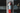 Red fire extinguisher mounted on a concrete wall with blurred lights in the background